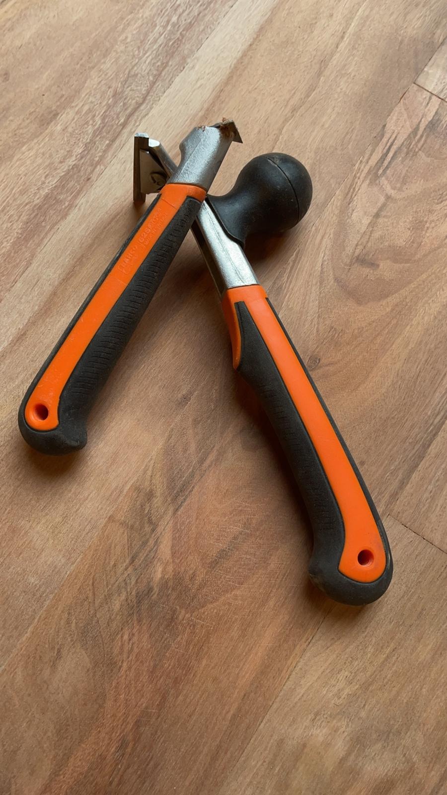 Dwa narzędzia do podważania i dobijania paneli podłogowych z czarno-pomarańczowymi uchwytami leżące na drewnianej podłodze.