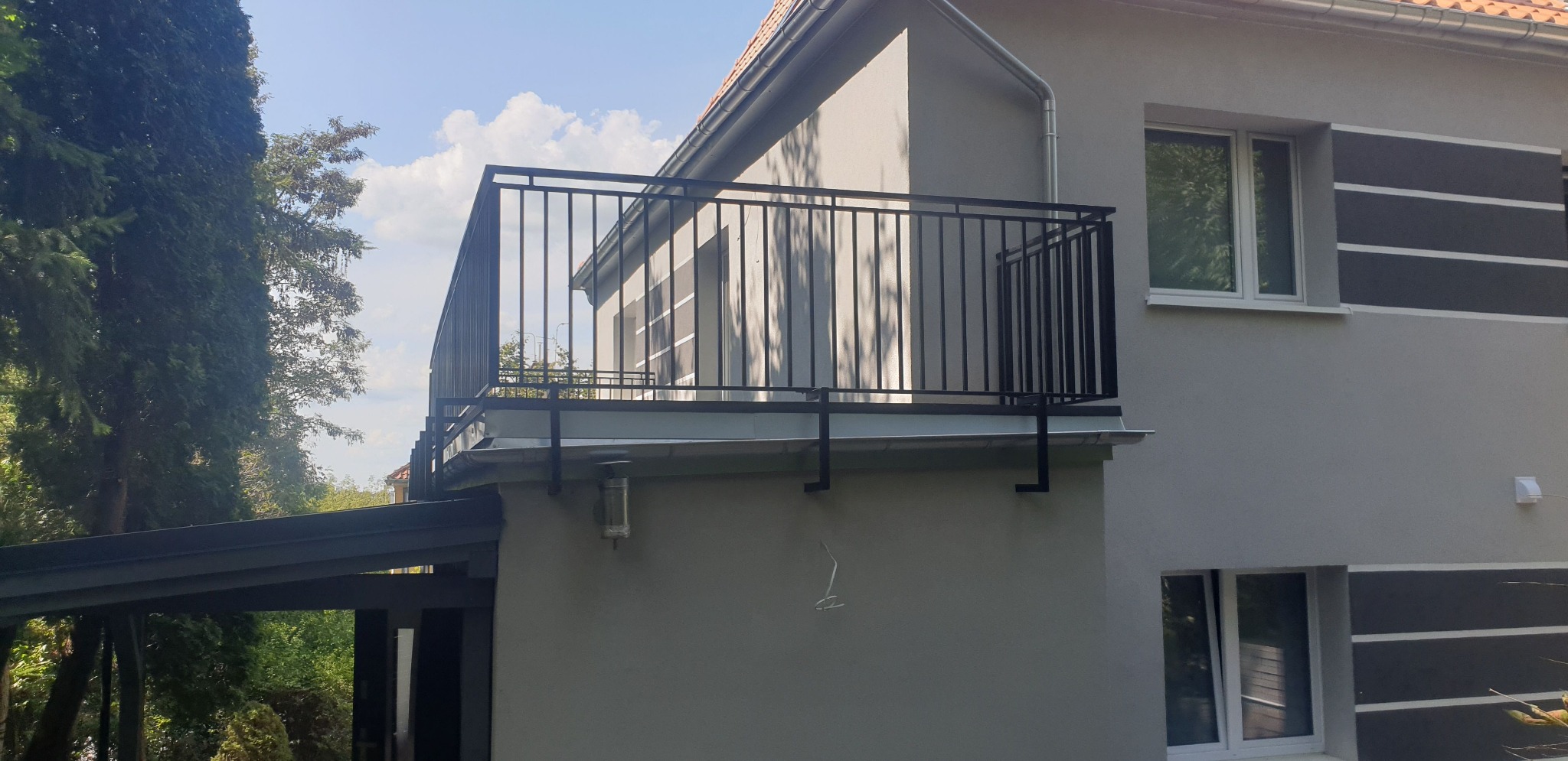 Czarna, metalowa balustrada balkonowa zamontowana na szarym budynku z dekoracyjnymi poziomymi pasami.