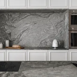 Nowoczesna kuchnia z szarym kamieniem na ścianie i blacie, białe szafki, piekarnik w zabudowie i biały czajnik SMEG.