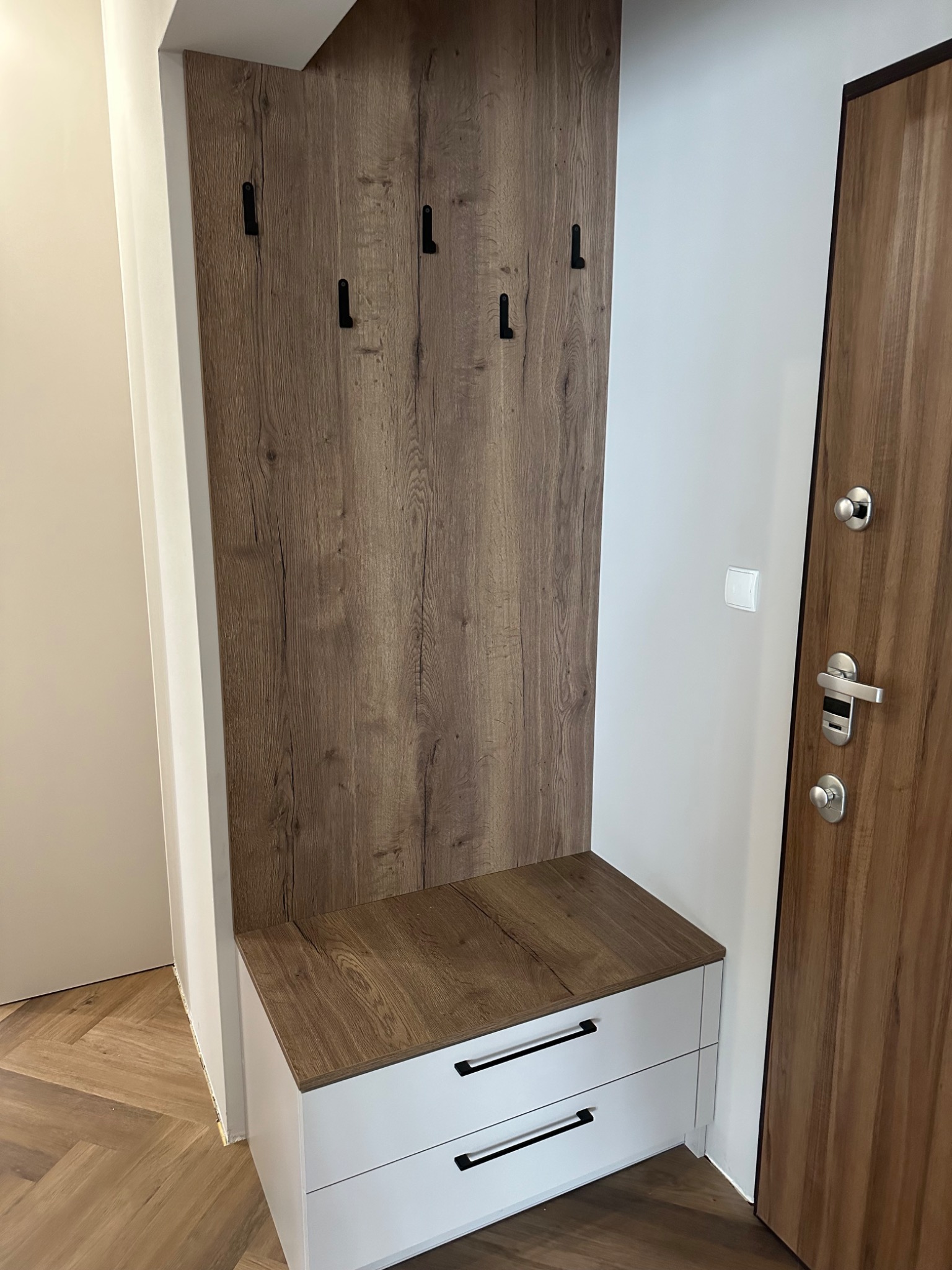 Wnęka z drewnianym panelem z wieszakami i białą szafką z dwoma szufladami w przedpokoju, widok z boku.