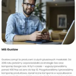 Uśmiechnięty mężczyzna w okularach i jeansowej koszuli siedzi przy biurku z laptopem i smartfonem w dłoniach, prezentujący ofertę firmy Gustaw.com.pl z tekstem o strategiach SEO i kampaniach Google...