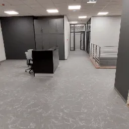 Biuro z szarą podłogą imitującą marmur, czarnymi regałami i recepcją, widok na korytarz z przeszklonymi drzwiami.