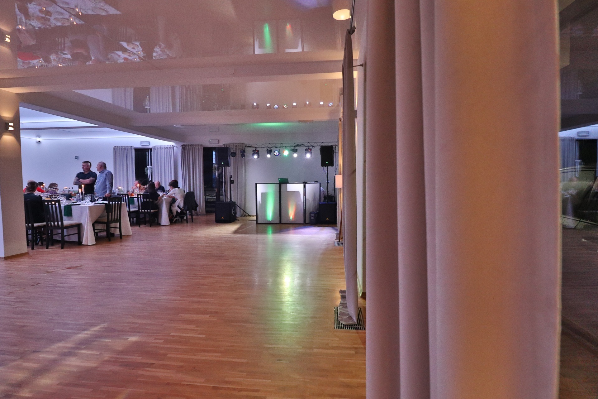 Sala bankietowa z ustawionymi stołami, oświetleniem scenicznym i dj-ką, widok zza kolumny.