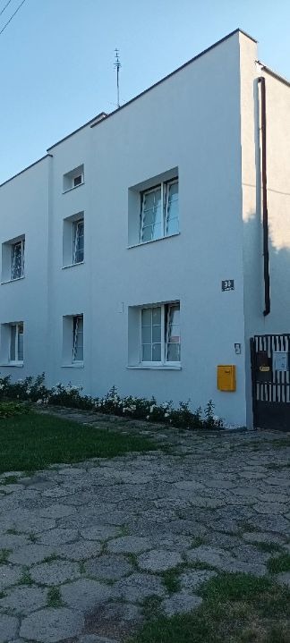 Dwukondygnacyjny budynek po odnowieniu elewacji, z widocznymi białymi ramami okiennymi, nową skrzynką pocztową i świeżo pomalowanym numerem domu na elewacji.