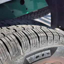 Szczegół opony busa z widocznym bieżnikiem i oznaczeniami: płatek śniegu, liść klonu, słońce, ptak.