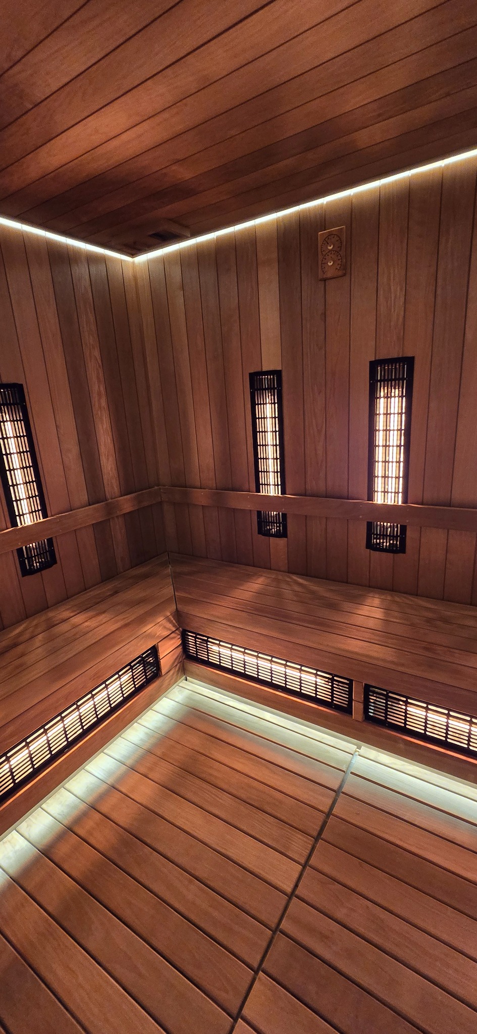 Wnętrze sauny infrared z drewnianym wykończeniem, oświetleniem LED i grzejnikami. Widok z góry na ławki i panele ścienne.