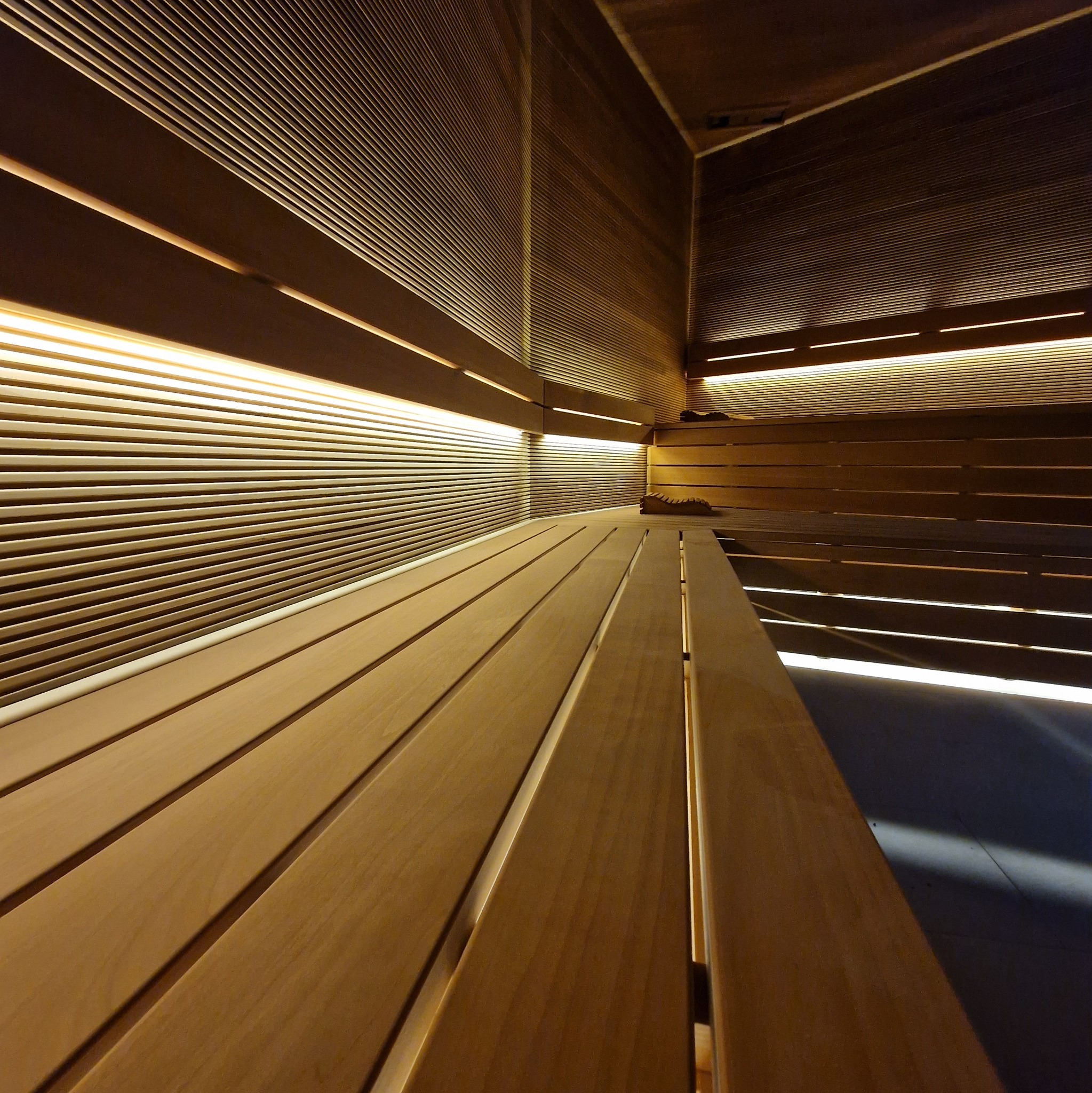 Drewniane wnętrze sauny z podświetlanymi panelami ściennymi i ławkami. Ujęcie z niskiej perspektywy podkreśla głębię i ciepło oświetlenia.