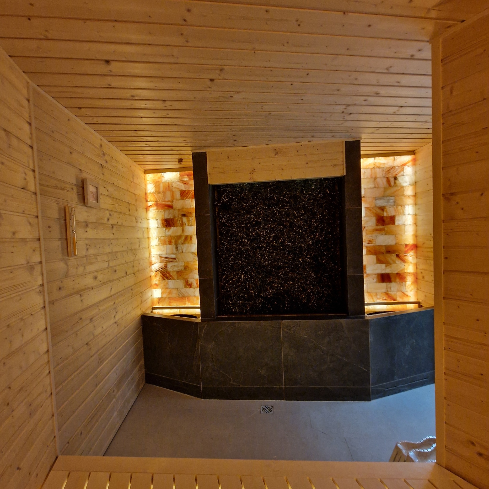 Drewniana sauna z tężnią solankową podświetloną od tyłu cegłami solnymi. Widok z góry na wnętrze, z widocznymi detalami wykończenia i oświetlenia.