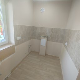 Fanabis Łukasz Biedziński - Wnętrze łazienki w trakcie układania płytek ceramicznych na podłodze i częściowo na ścianach, widoczna wentylacja sufitowa, okno z widokiem na zewnątrz, niedokończone prace wykończeniowe.