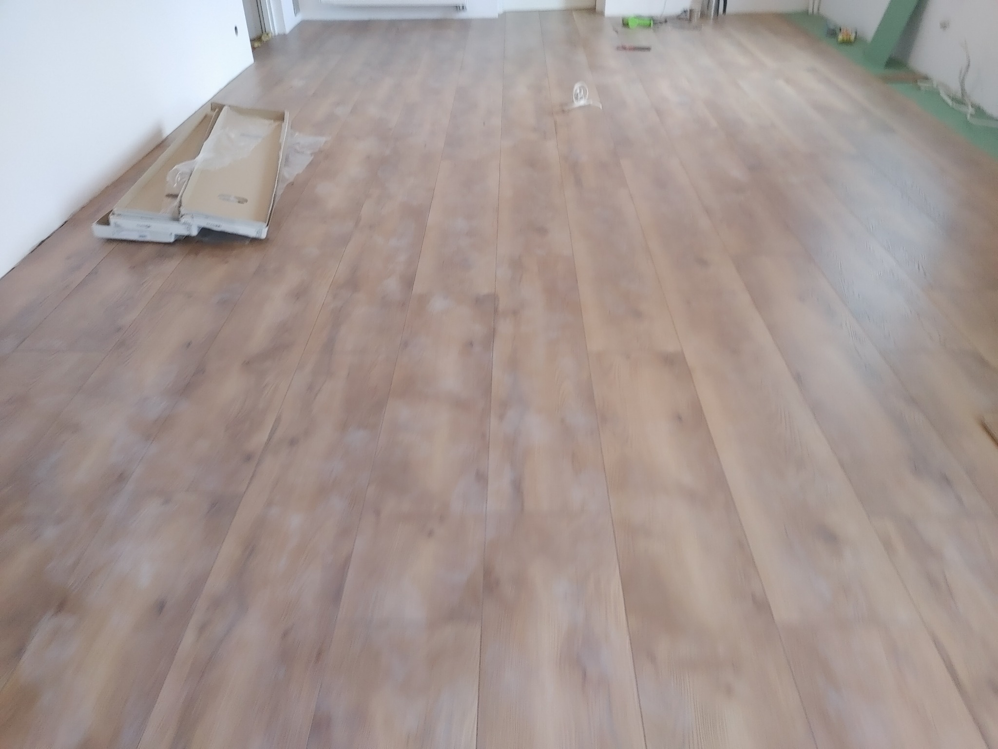 Ułożone panele podłogowe w trakcie prac wykończeniowych, widoczne kartony paneli przy ścianie i resztki materiałów budowlanych w tle.