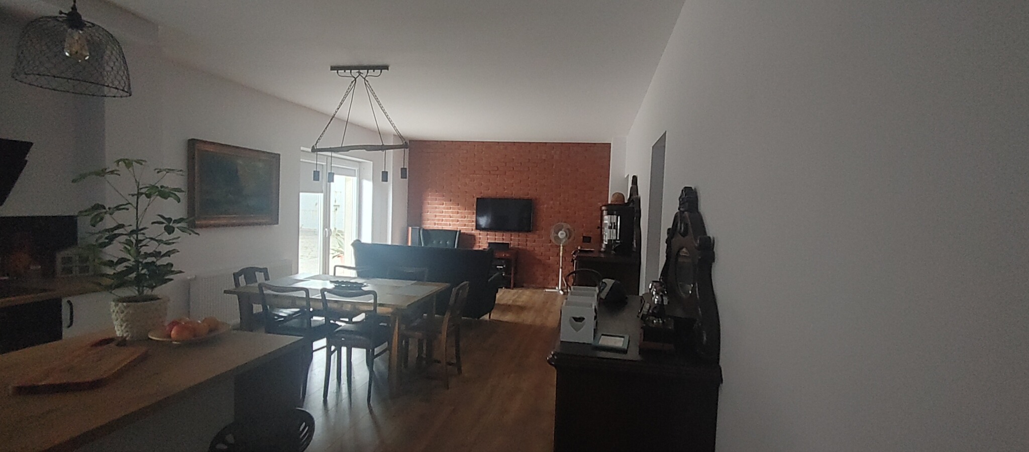 Przestronny salon z ceglaną ścianą, drewnianym stołem i ozdobnym oświetleniem, widok z perspektywy wejścia.