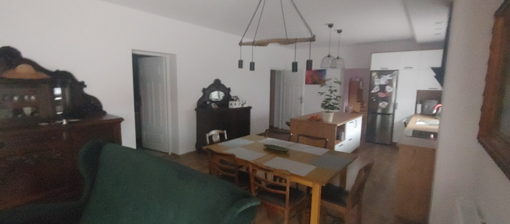 Przestronne wnętrze mieszkania w Grudziądzu po odświeżeniu, z widoczną jadalnią, elementami kuchni i odnowionymi ścianami, oświetlone lampą wiszącą z drewnianym elementem.