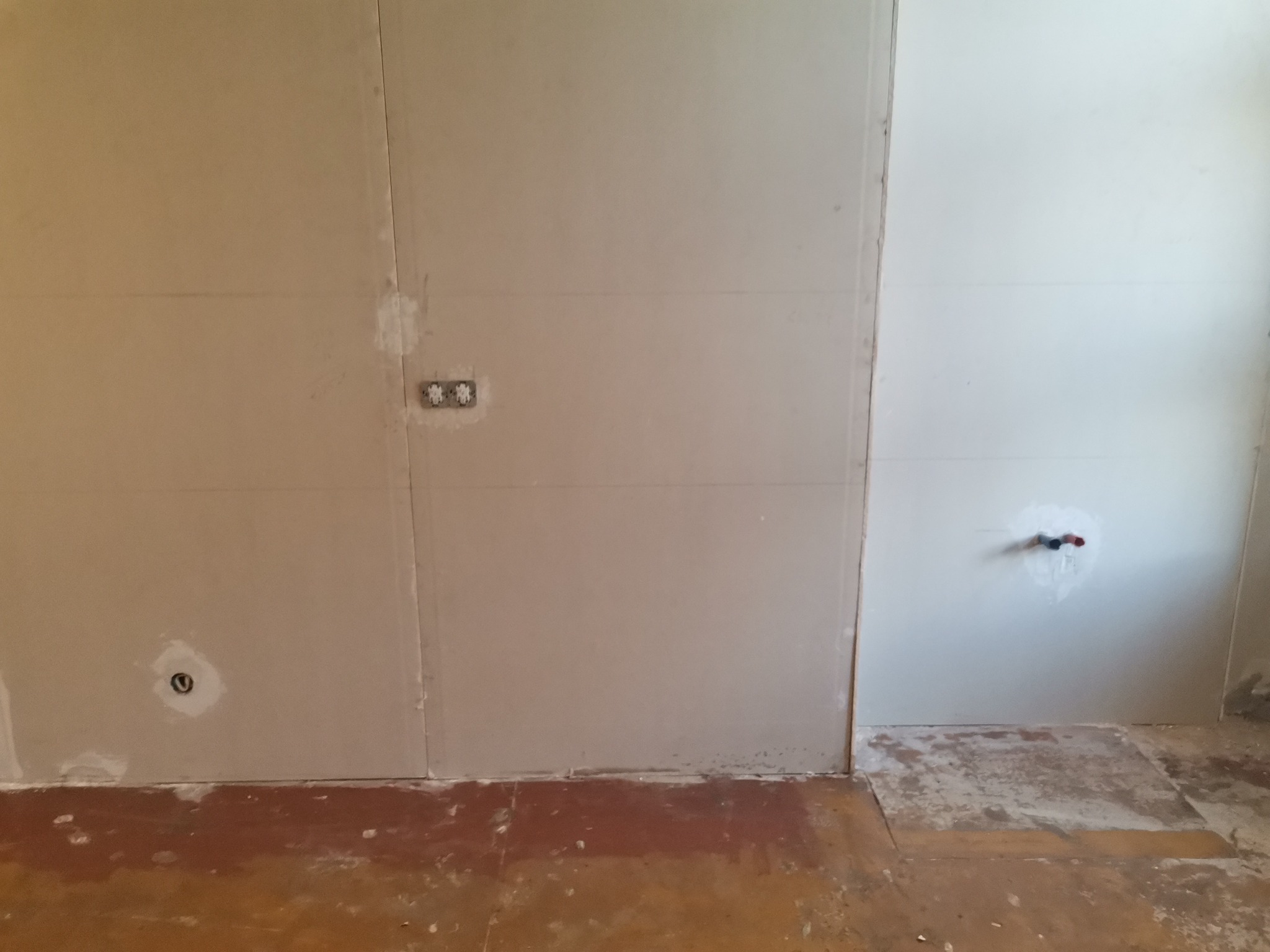 Ściana z płyt kartonowo-gipsowych przed położeniem gładzi, widoczne puszki elektryczne i rury wodne, przygotowywane do dalszych prac wykończeniowych.