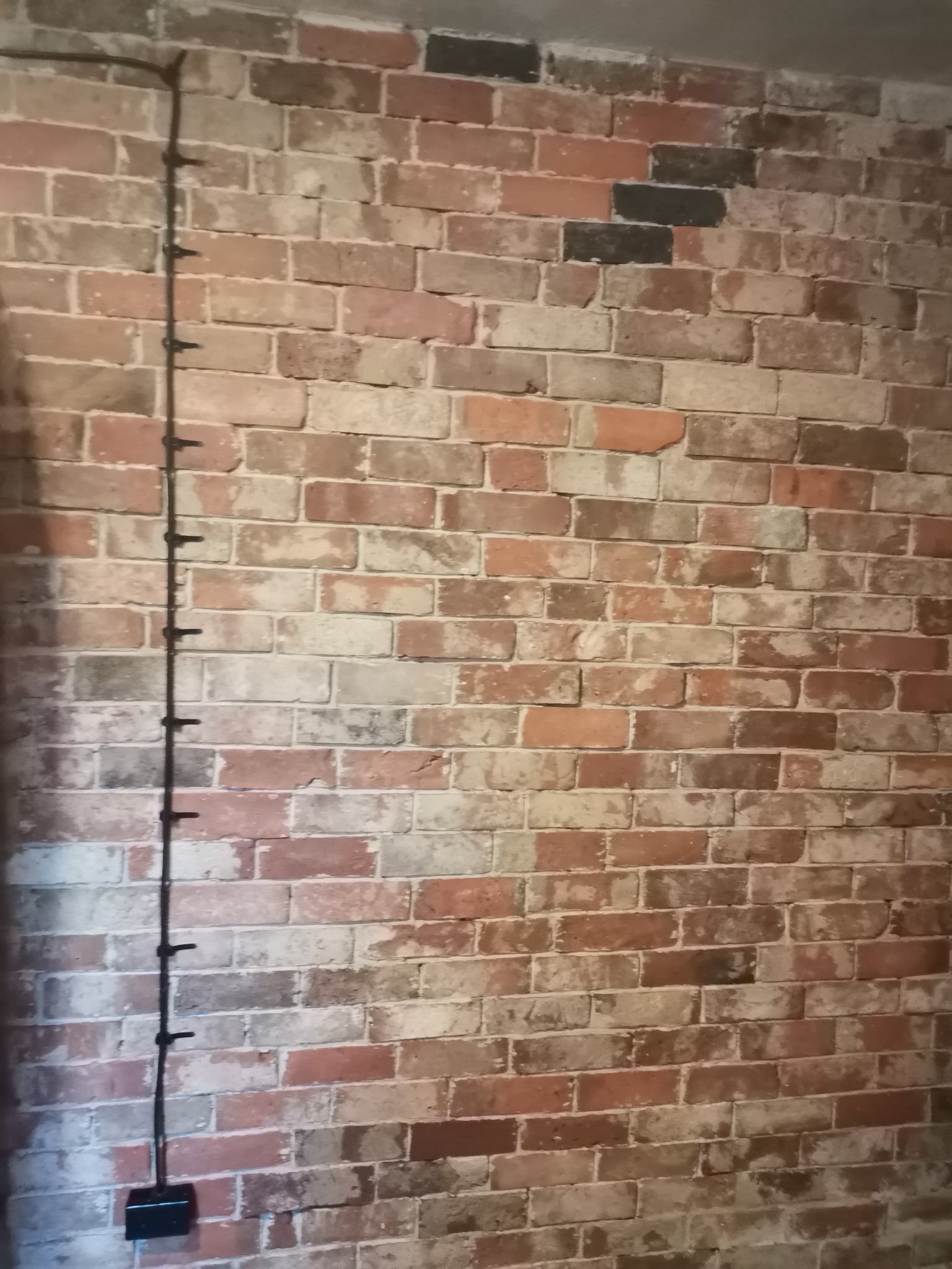 Ściana z cegły dekoracyjnej w odcieniach czerwieni, brązu i szarości z pionowo poprowadzonym kablem elektrycznym mocowanym za pomocą uchwytów.