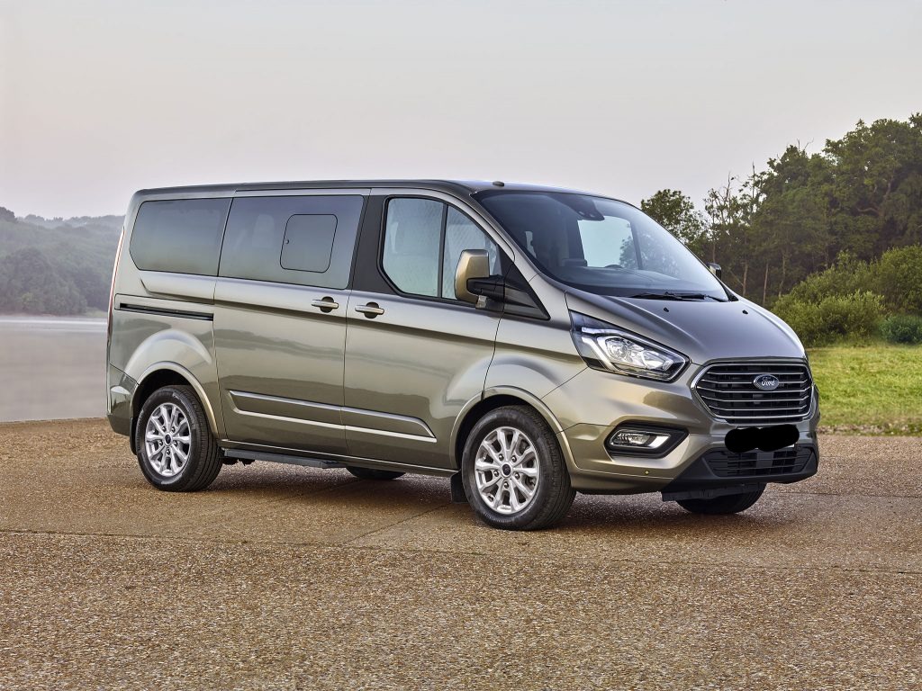 Szaro-złoty samochód dostawczy Ford Transit Custom w Drzonkowie, zaparkowany na betonowej nawierzchni z widokiem na zieleń w tle.