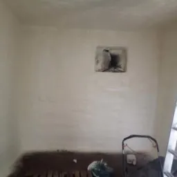 Wnętrze pomieszczenia po nałożeniu izolacji, widoczna drabina oparta o ścianę i otwór wentylacyjny zakryty folią.