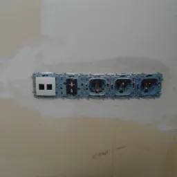 Nierówna ściana w trakcie szpachlowania w Częstochowie z zamontowanymi puszkami pod gniazdka i włącznik światła, widoczne przewody elektryczne.
