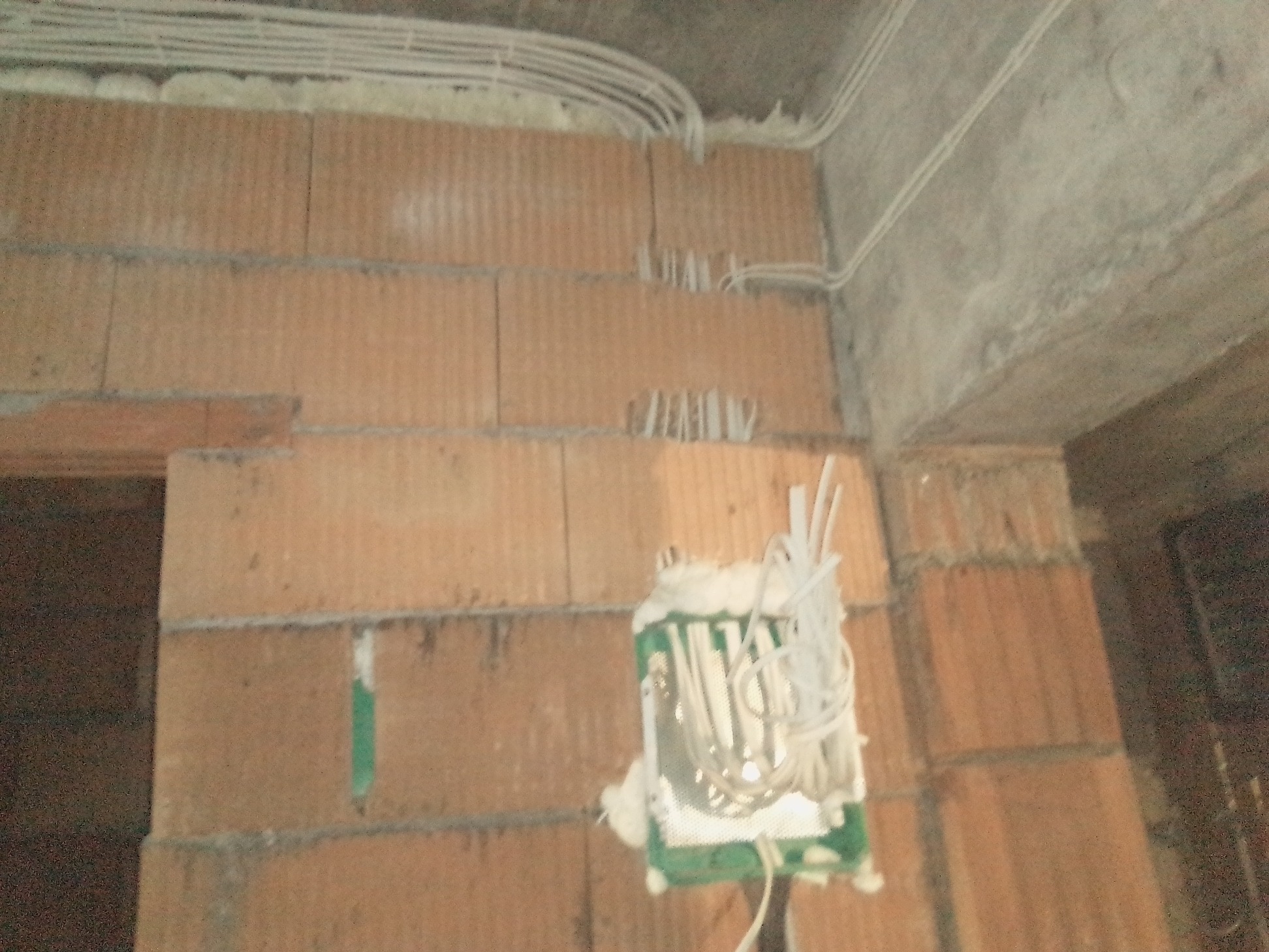 Wewnętrzna instalacja elektryczna w surowym murze z cegły, widoczne kable w peszlach i puszka instalacyjna zabezpieczona pianką montażową.