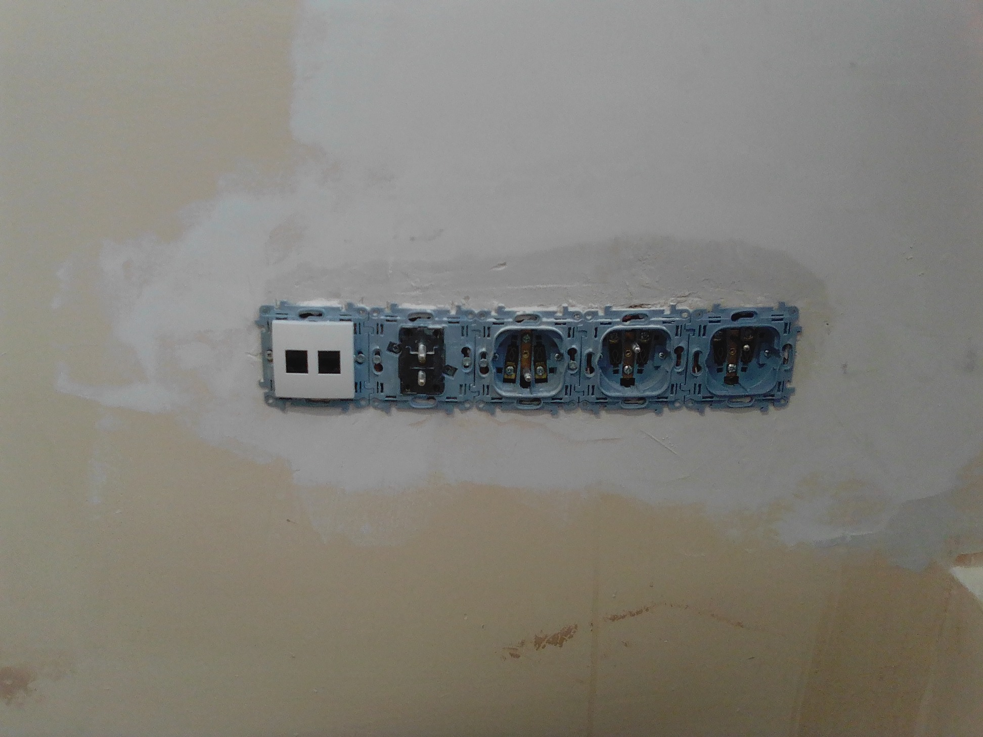 Nierówna ściana w trakcie szpachlowania w Częstochowie z zamontowanymi puszkami pod gniazdka i włącznik światła, widoczne przewody elektryczne.