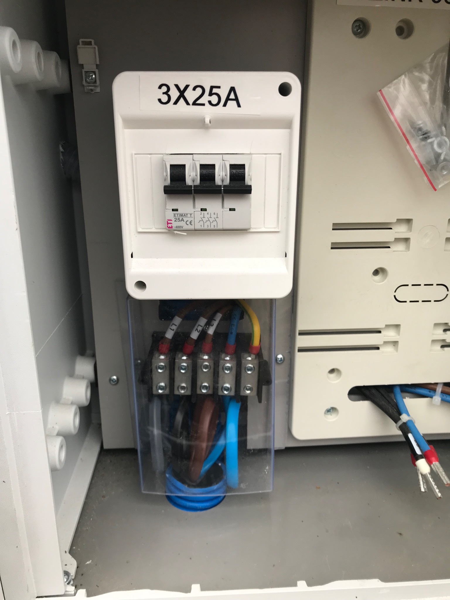 Szczegółowe ujęcie rozdzielnicy elektrycznej z bezpiecznikami 3x25A i podłączonymi przewodami w skrzynce, zrealizowane w Ostródzie.