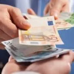 Dwie dłonie wymieniające plik banknotów euro o różnych nominałach na rozmytym, niebieskim tle.