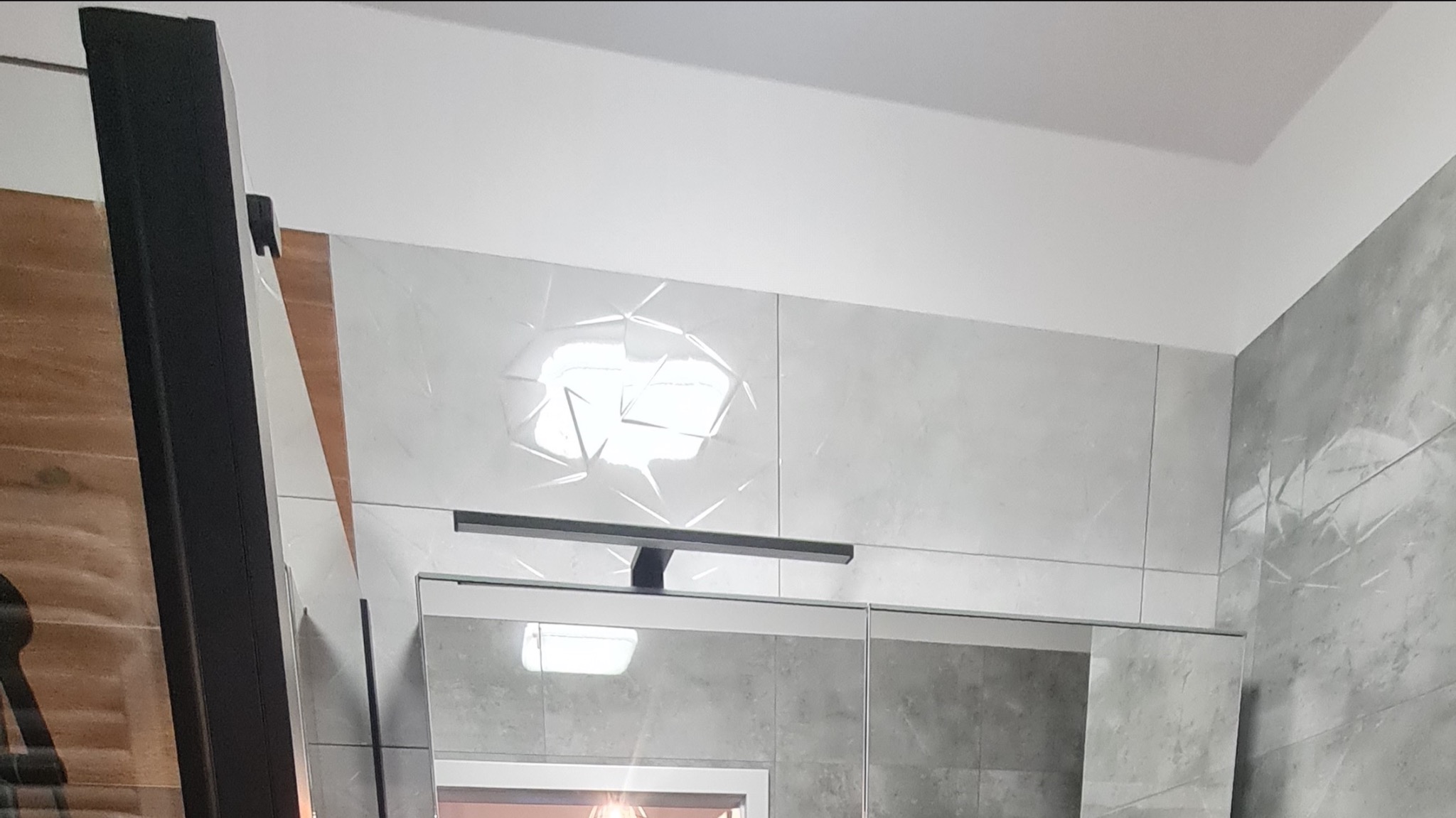 Nowoczesna łazienka z szarymi płytkami imitującymi beton i dekoracyjnymi płytkami 3D, oświetlenie nad lustrem