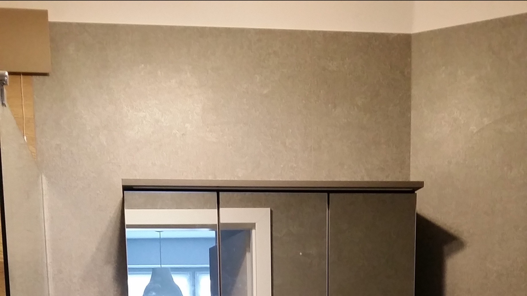 Szara ściana z efektem dekoracyjnym, szafka łazienkowa z lustrem i widocznym oświetleniem w odbiciu.