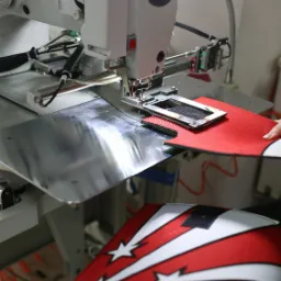 Automat szwalniczy podczas pracy nad czerwono-białym materiałem z motywem gwiazd i smug, zbliżenie na igłę i uchwyt materiału.