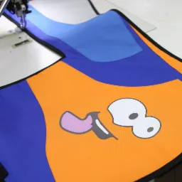 Szwalnia: Fragment kolorowego pokrowca z nadrukiem postaci z kreskówki, szytego na maszynie do szycia.