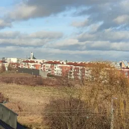 Widok na osiedle mieszkaniowe z nowym dachem z blachy trapezowej na pierwszym planie, w tle budowa z żurawiem i kościół.