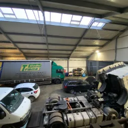 Warsztat w Szamocinie z kilkoma pojazdami, w tym ciężarówką z otwartą maską podczas naprawy, oraz zaparkowanymi samochodami osobowymi i dostawczymi.