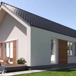 Nowoczesny dom parterowy z ciemną dachówką, drewnianymi akcentami elewacyjnymi i tarasem z białymi kwiatami w donicach, otoczony zielonym trawnikiem i drzewami.