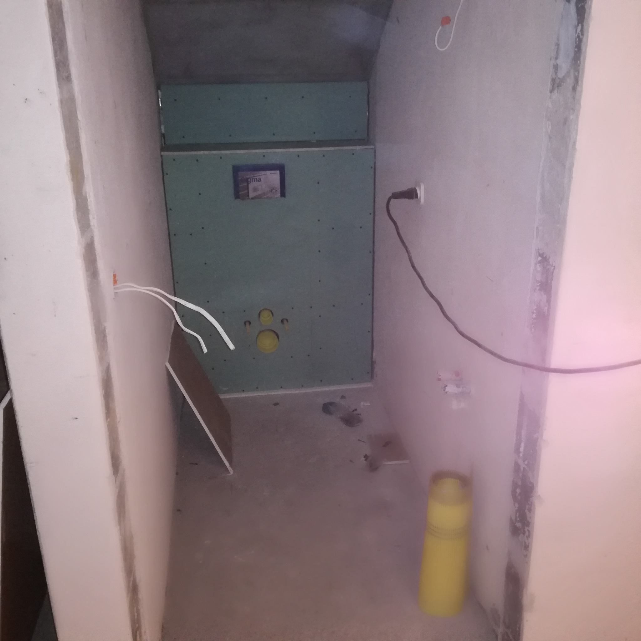 Przygotowanie do montażu podtynkowego stelaża WC: płyta kartonowo-gipsowa z widocznymi otworami na rury, przewody elektryczne i częściowo wykończone ściany w surowym stanie.