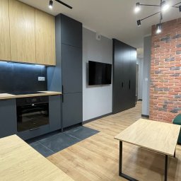 VLADISLAV RZHANSKY - Nowoczesne wnętrze: szara zabudowa kuchenna z drewnianymi szafkami, ceglana ściana, drewniana podłoga i stół. Minimalistyczny design z oświetleniem LED.