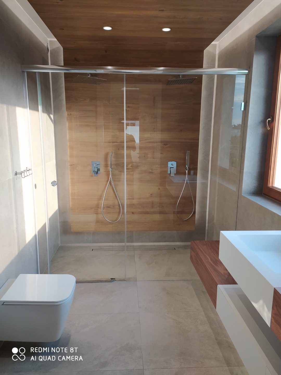 Nowoczesna łazienka z kabiną prysznicową typu walk-in, drewnianym wykończeniem ścian i sufitu, oraz minimalistyczną umywalką nablatową.