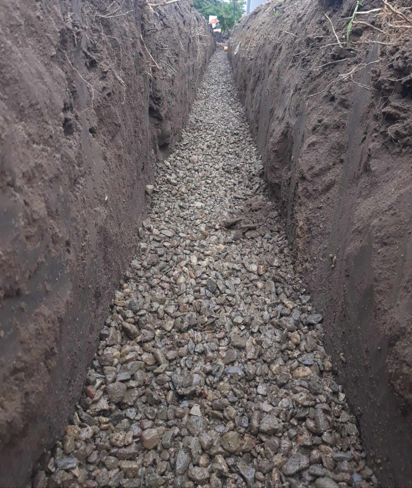 Wykop wypełniony żwirem, widoczne ściany z ciemnej ziemi, perspektywa w głąb wykopu.