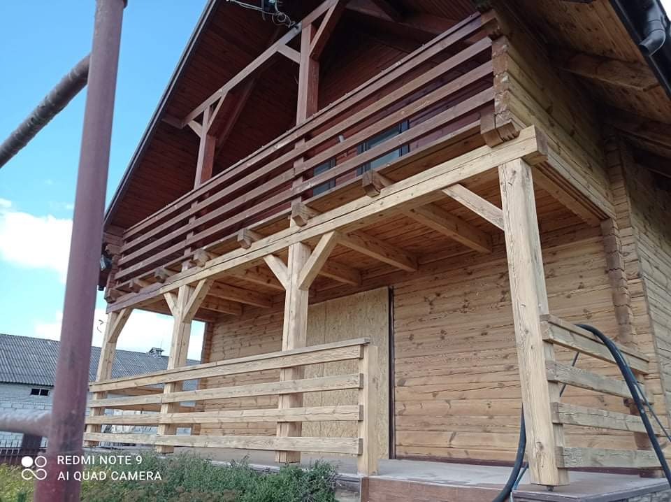 Drewniany dom z balkonem po zabezpieczeniu i malowaniu, widoczne świeże drewno i konstrukcja wsporcza.