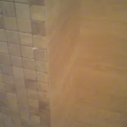 Ściana wykończona mozaiką ceramiczną w odcieniach beżu i brązu, sąsiadująca z powierzchnią pokrytą dekoracyjnym tynkiem w ciepłym, piaskowym kolorze. Widoczny fragment narożnika pomieszczenia.