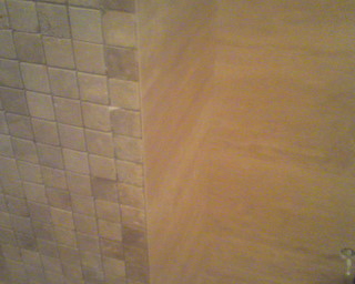 Ściana wykończona mozaiką ceramiczną w odcieniach beżu i brązu, sąsiadująca z powierzchnią pokrytą dekoracyjnym tynkiem w ciepłym, piaskowym kolorze. Widoczny fragment narożnika pomieszczenia.