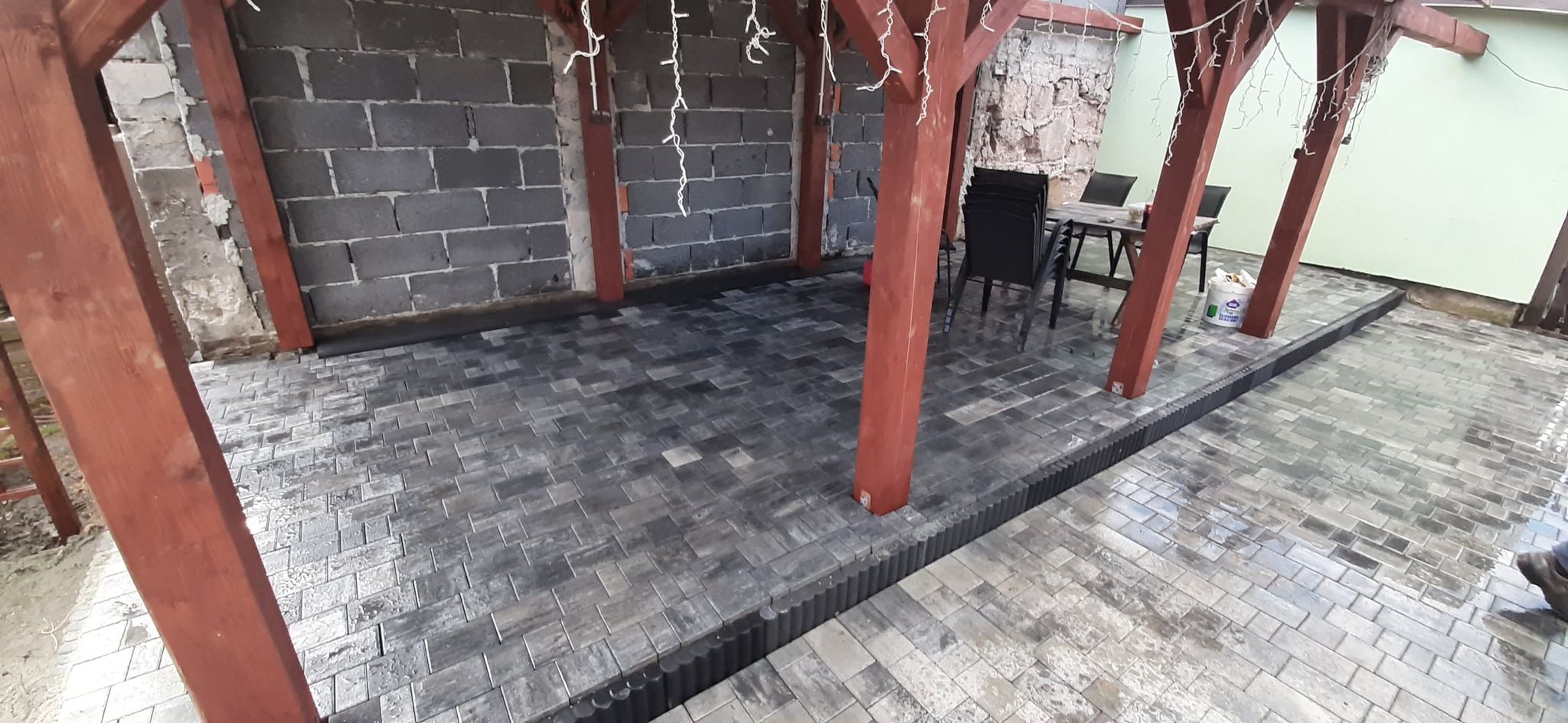 Nowo ułożona, szara kostka brukowa w ogrodowej altanie z drewnianą konstrukcją, widoczne elementy dekoracyjne i meble ogrodowe.