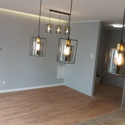 Nowoczesne oświetlenie w szaro-beżowym wnętrzu z panelami podłogowymi i minimalistycznymi lampami wiszącymi