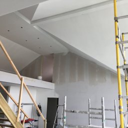 Dawid Fornal - Wnętrze w trakcie prac wykończeniowych: ściany przygotowane do malowania, widoczne szpachlowanie, rusztowania, drewniane schody w surowym stanie, sufit z elementami dekoracyjnymi i punktami...