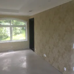 Pusty pokój po remoncie z ozdobną tapetą w odcieniach beżu, dużym oknem łukowym i wylewką samopoziomującą na podłodze.