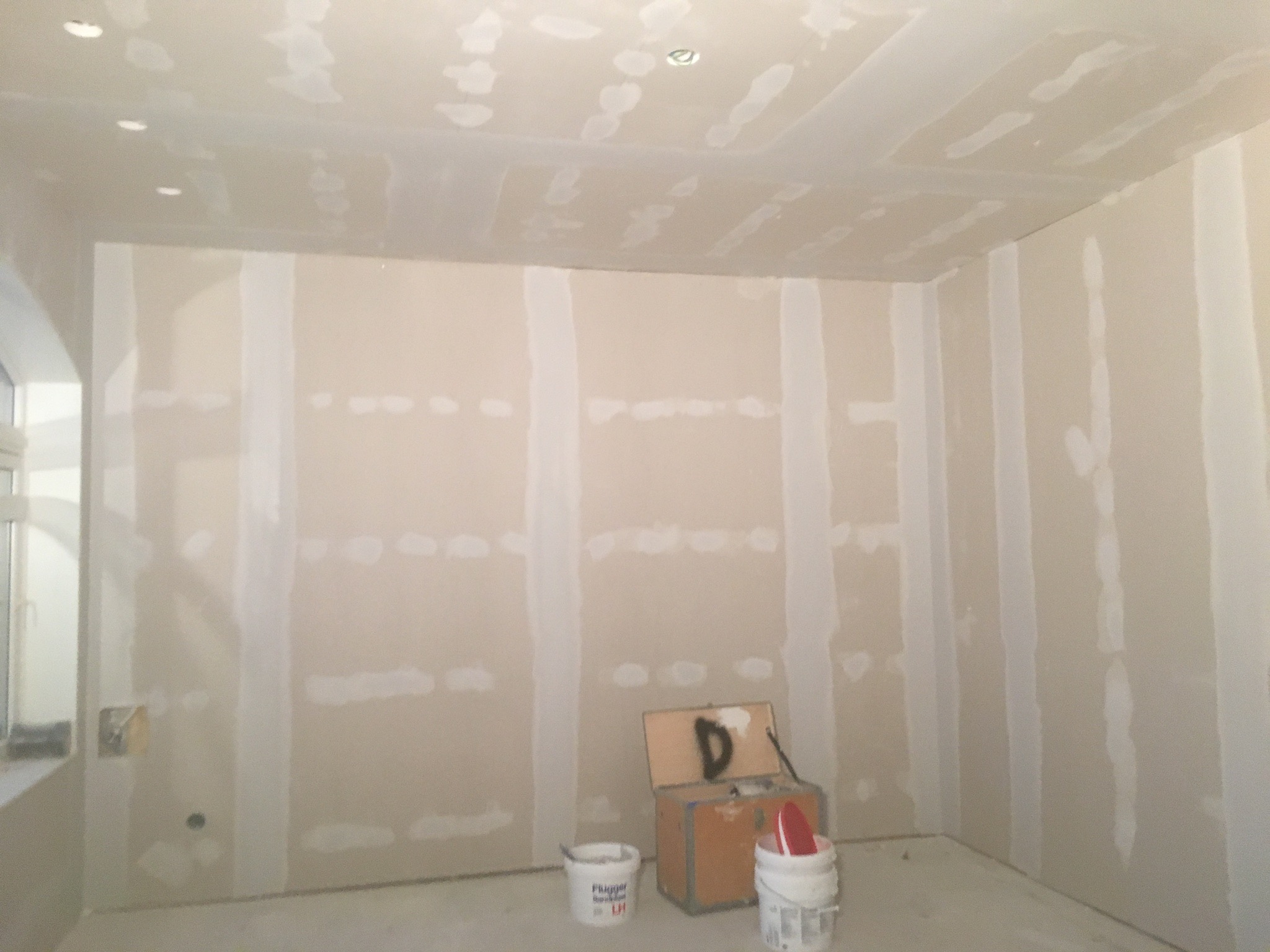 Pokój w trakcie prac przygotowawczych do malowania, widoczne ściany pokryte gładzią szpachlową, skrzynka narzędziowa z pędzlem i dwa wiadra z masą szpachlową.