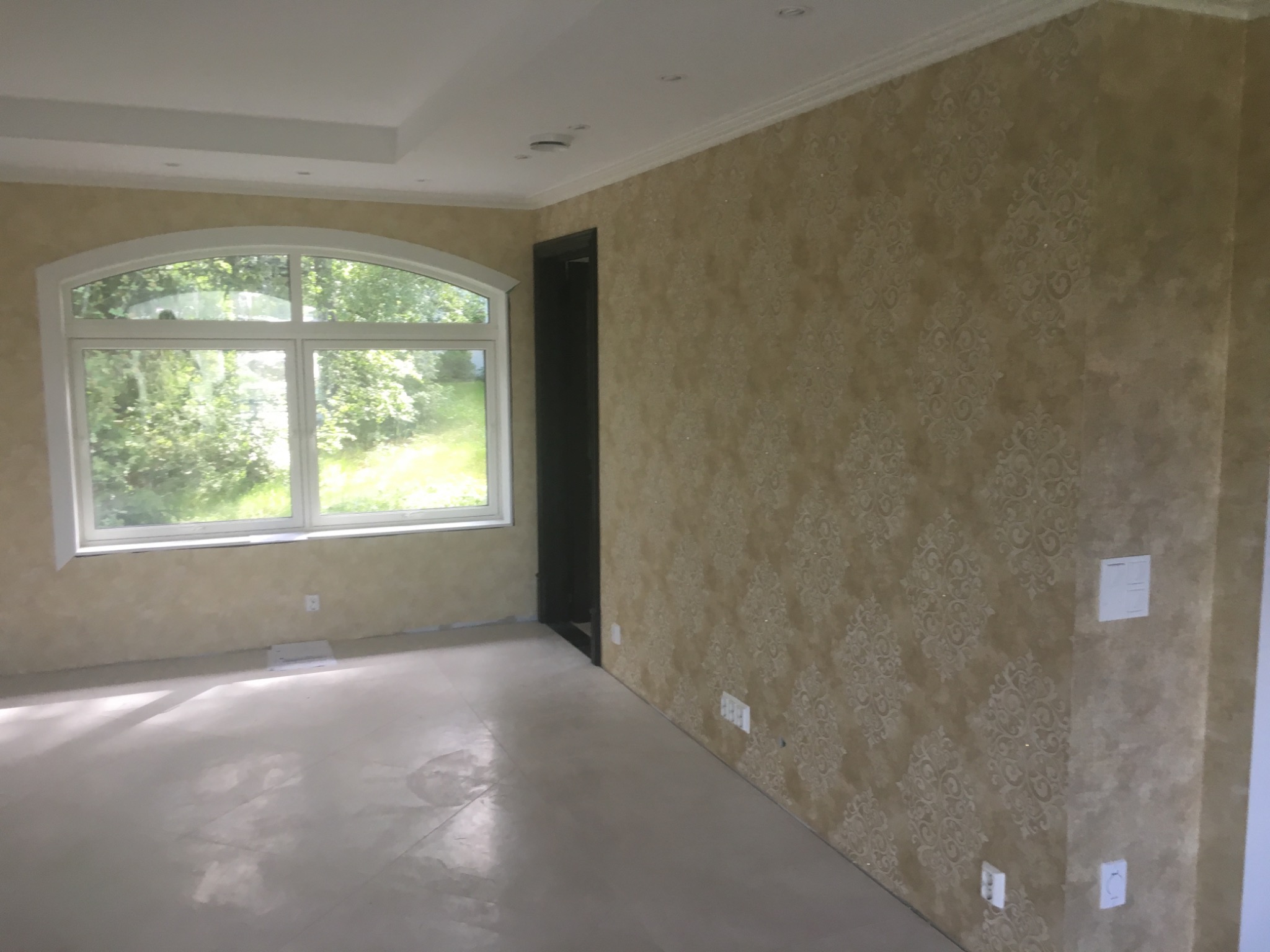 Pusty pokój po remoncie z ozdobną tapetą w odcieniach beżu, dużym oknem łukowym i wylewką samopoziomującą na podłodze.