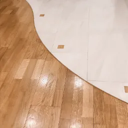 Parkiet dębowy płynnie przechodzący w jasne płytki ceramiczne z dekoracyjnymi wstawkami z drewna, tworząc falisty wzór podłogi.