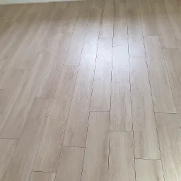 Jasne, drewnopodobne panele ułożone na podłodze w nowym pomieszczeniu, widoczny grzejnik na ścianie i wystająca rurka instalacji grzewczej.