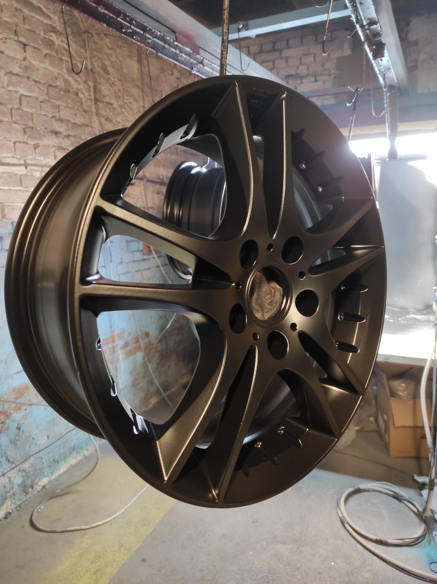 Pomalowana proszkowo felga aluminiowa zawieszona na haku w warsztacie, widoczne detale konstrukcji i matowe wykończenie farby.