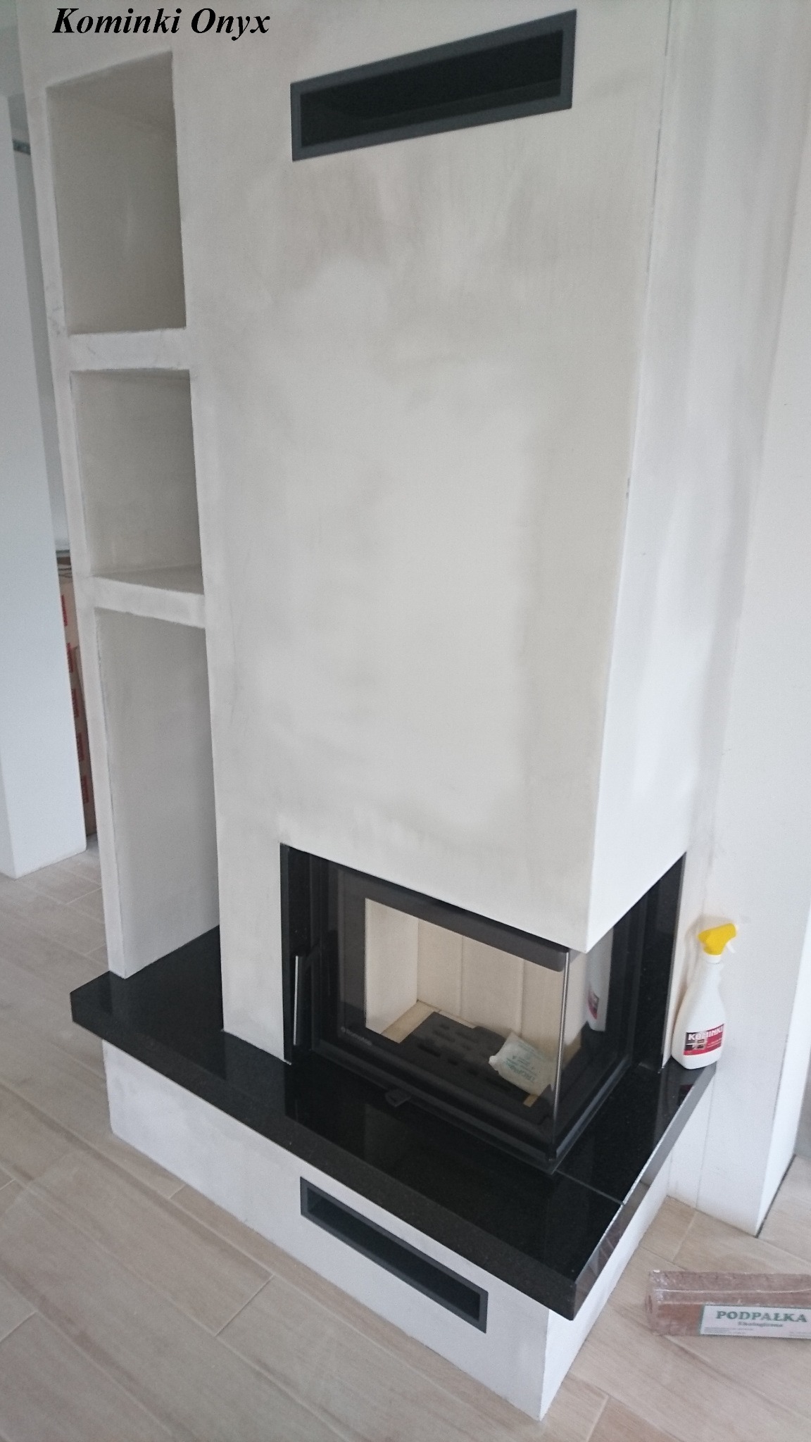 Nowoczesny, biały piec z czarnym blatem z kamienia, w trakcie wykańczania, widoczna butelka płynu do czyszczenia i podpałka.