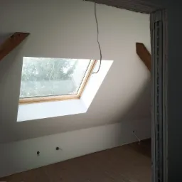 Poddasze po ociepleniu z oknem dachowym, widoczne elementy konstrukcyjne i instalacje elektryczne, ściany wykończone płytą karton gips.